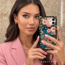 Load image into Gallery viewer, Woman holding a luxury iPhone case with floral design by PURITY in front of a mirror.
