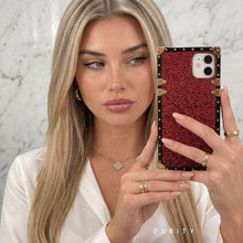 Load image into Gallery viewer, Woman holding a luxury red glitter phone case with gold accents against a marble background

